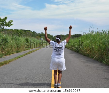 Mature Woman Fists Raised American Healthcare for Ransom on Tee Shirt Back to Camera Standing on Street Yellow Traffic Line