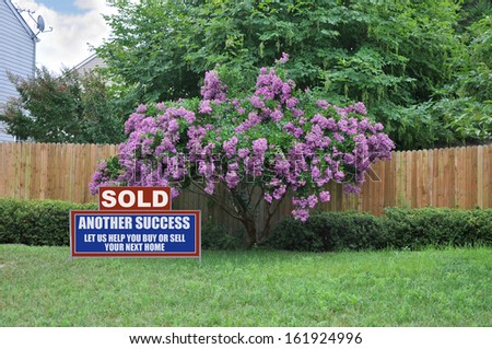 Sold Real Estate Sign Lawn of Suburban Home with Blooming Tree Wood Fence
