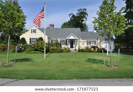 American Flag pole suburban ranch style home landscaped flowers plants trees sunny blue sky day residential neighborhood usa