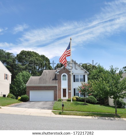 American Flag pole suburban mcmansion style home residential neighborhood usa blue sky clouds