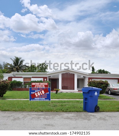 Sold Real Estate Sign (Another Success Let us help you buy / sell your next home) Recycle Trash Can curbside suburban ranch style home residential neighborhood USA blue sky clouds