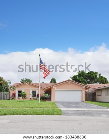 American Flag Pole front yard lawn of Suburban Ranch Back split style home residential neighborhood USA Blue Sky Clouds