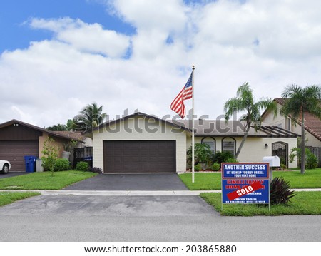 Sold Real estate sign (another success let us help you buy sell your next home)  Suburban Ranch Home Two Car Garage Landscaped front yard residential neighborhood USA blue sky clouds