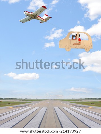 Airplane flying over airport runway with boy in card board car looking through binoculars