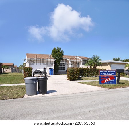 Real Estate Sold (another success let us help you buy sell your next home) sign on front yard lawn of suburban ranch style home residential neighborhood sunny blue sky clouds USA