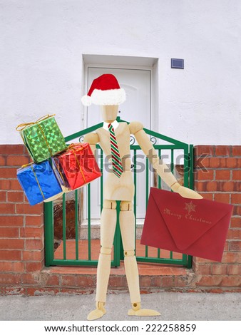 Santa Mannequin holding Christmas gifts and xmas card with Merry Christmas in front of Home Entrance Gate Brick wall