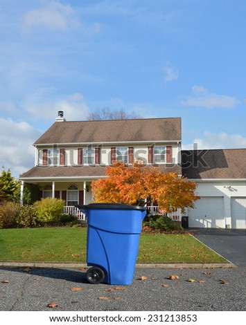 Blue Trash Recycle Container on suburban street in front of colonial style home autumn day residential neighborhood blue sky clouds USA
