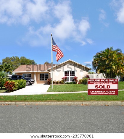 American flag pole Real Estate sold (another success let us help you buy sell your next home) sign suburban ranch style home sunny residential neighborhood blue sky clouds USA