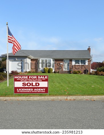 American flag pole Real Estate Sold (another success let us help you buy sell your next home) sign suburban ranch style home residential neighborhood blue sky clouds USA