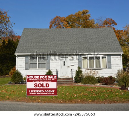Real estate sold (another success let us help you buy sell your next home ) sign front yard Suburban white and gray cape cod style home autumn day clear blue sky residential neighborhood USA