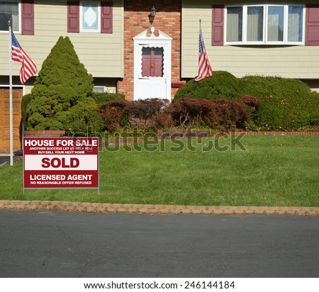 American flag pole Real estate sold (another success let us help you buy sell your next home) sign Suburban High Ranch home with cobble stone curb sunny autumn day residential neighborhood USA