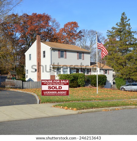 American flag pole Real estate sold (another success let us help you buy sell your next home) sign Suburban high ranch home autumn clear blue sky day residential neighborhood USA