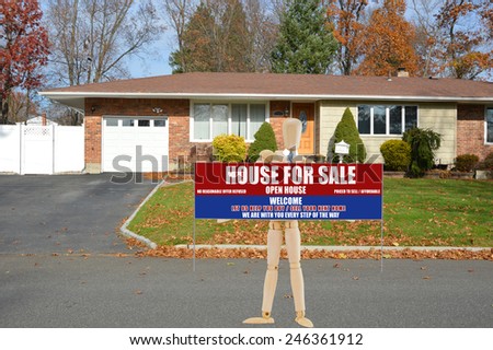 Mannequin holding Real estate for sale open house welcome sign suburban brick ranch style home white picket fence blacktop driveway autumn blue sky day residential neighborhood USA
