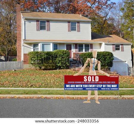 Mannequin holding Real estate sold (another success let us help you buy sell your next home) sign Suburban Tan High Ranch home with leaves on front lawn autumn day residential neighborhood Sunny sky