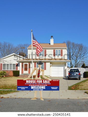 American flag pole mannequin wearing businessman attire holding Real estate for sale open house welcome sign Suburban home burnt dry front yard lawn blue sky residential neighborhood autumn day USA