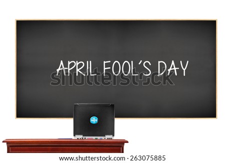Blackboard with April Fool\'s Day behind desk with computer Prankster sticker button isolated on white background
