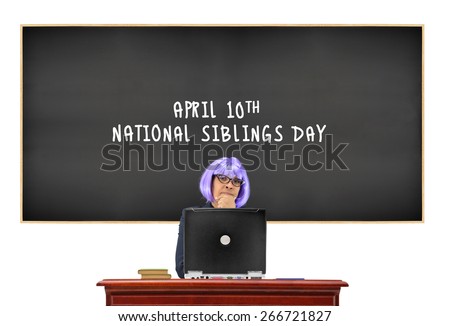 Teacher behind computer on classroom desk with April 10th National Siblings Day Blackboard isolated on white background
