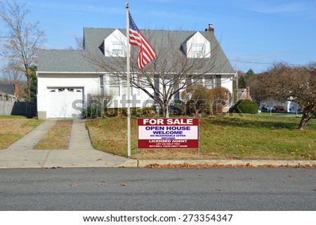 Real estate for sale open house welcome sign Suburban Cape Cod style home sunny blue sky autumn day residential neighborhood USA American Flag pole