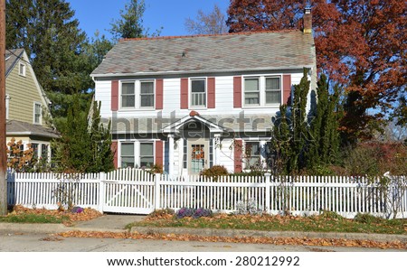 Beautiful Suburban Colonial Home with white picket fence autumn clear blue sky day residential neighborhood USA