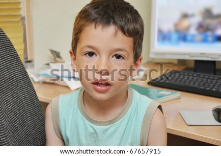 Handsome Little Preschool Boy Sitting at Office Desk in front of Computer Looking at Camera