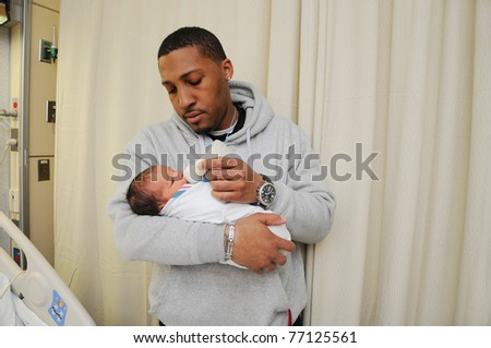 New Tired Family Father Holding Feeding Newborn Infant Baby in Hospital Room Just after Birth