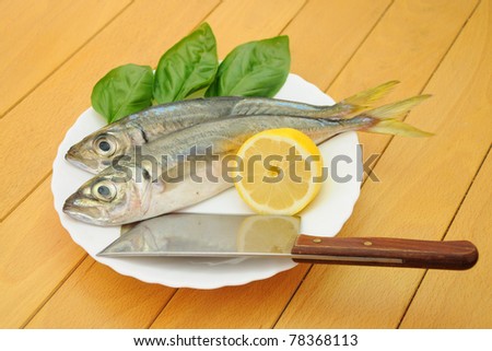 Two Fresh Whole Spanish Mackerel Fish on Plate with Basil Leaves Lemon Half and Butcher Knife