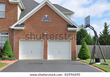 Basketball Hoop on Driveway in front of Suburban Home Two Car Garage Doors on Sunny Day