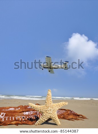 Small Airplane flying over mediterranean beach with starfish and sarong laying on sand