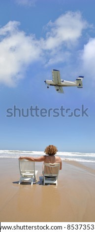 Woman sitting on Mediterranean beach next to Empty Chair Airplane Flying by Blue Sky Day Costa Blanca Alicante Spain Europe