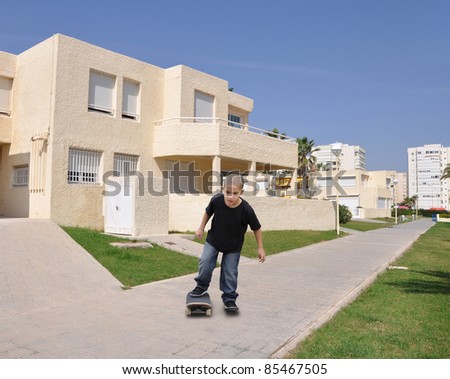 School Age Boy Skateboarding on Apartment Complex Sidewalk under Clear Sunny Blue Sky Day