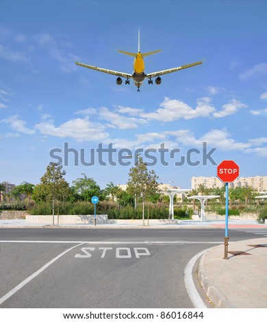 Airplane Flying over Urban City Street with Traffic Stop Sign on Sunny Blue Sky Day