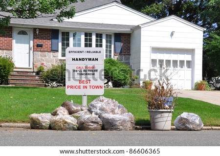 Handyman Sign on Front Yard Lawn of Suburban Home behind Plastic Bags of Trash on Street Curb in Residential Neighborhood