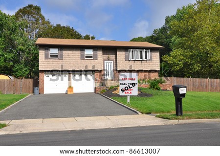 Realtor Sold Sign on Suburban Ranch Style Two Car Garage Home in Residential Neighborhood on Sunny Cloudy Blue Sky Day