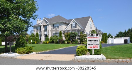 Sold Relocation For Sale Sign on Front Yard Landscape Area of Suburban Brick McMansion Home in Residential Neighborhood on Sunny Blue Sky Day