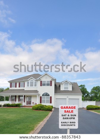 Garage Sale Sign at Driveway edge of large two car garage suburban home on sunny blue cloud sky day in residential neighborhood