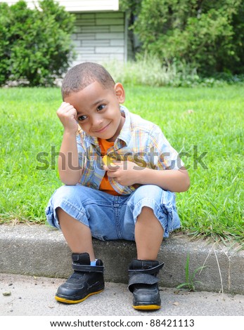 Handsome Little Boy Daydreaming Smiling Hand on Head sitting on curb of suburban home during daytime