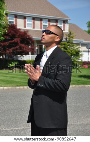 Young man praying in street in front of suburban home on sunny blue sky day