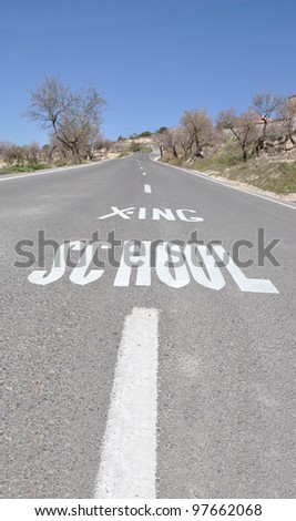 School Crossing Street Sign on Blacktop Pavement Road lined with Almond Trees in Bloom clear blue sky day