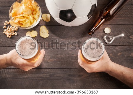 two glasses of beer in men\'s hands. Chin-chin. Top view