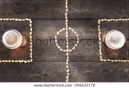 Two glass of beer on a miniature football field markings of peanuts. top view