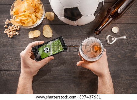 man with beer watching soccer game on smartphone. Top view
