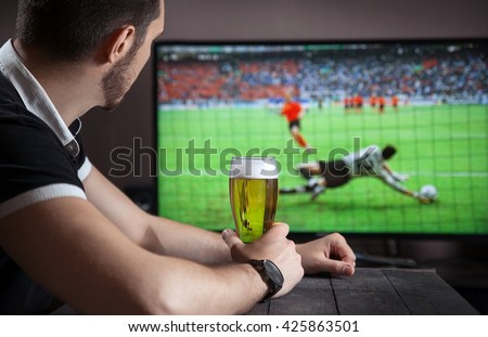 Men with glass of beer watch soccer match in bar.
