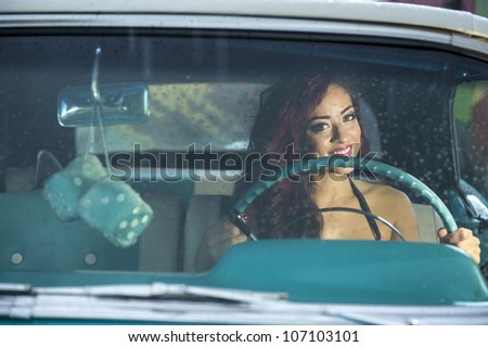 Young woman driving classic car in the rain.