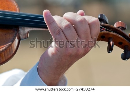 Close-up of hands playing violin outdoors during a concert.