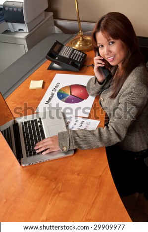 Young woman talking by phone and working on computer in small office.