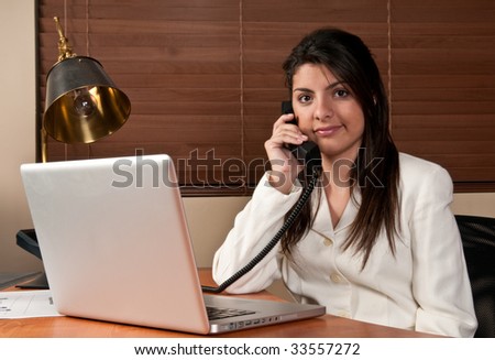 Young woman working in a small office and talking by phone.