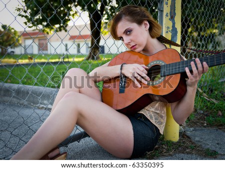 Young woman playing guitar outdoors. Space for copy.