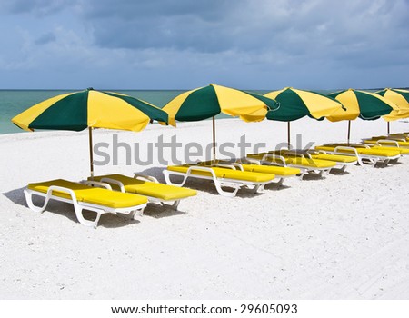 A series of yellow lounge chairs with green and yellow parasols, on a pristine white sand beach.