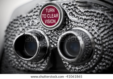 The knob that reads turn to clear vision, on pay binoculars. Closeup view and slightly desaturated image.