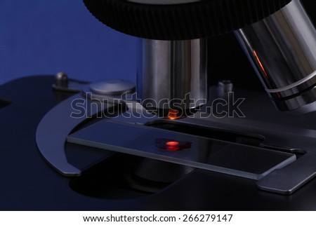 The drop of a red liquid illuminated on a slide of a dark microscope